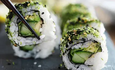 Close up photo of vegan sushi rolls. One piece is being picked up by chopsticks.