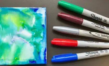 Five colored Sharpies to the right of a tie-dye tile coaster