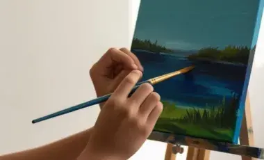 a hand using a brush to paint on canvas