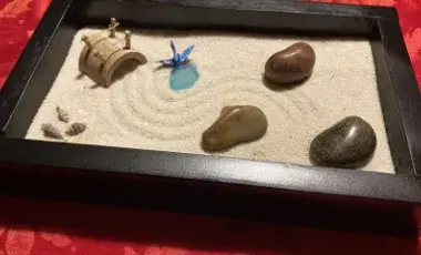 mini Zen garden made of a wooden lacquer tray filled with sand and decorated with river stones, shells and bamboo bridge. A swirling pattern in the sand has been created with a rake.