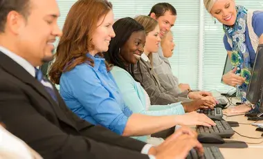 Woman seen instructing row of adults seated at computers