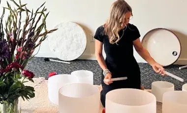 A woman in a black dress performs using seven quartz bowls laid out in front of her