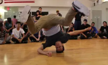 Breakdance with head on the ground and people looking on in a gym
