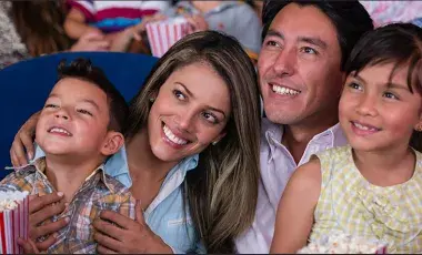 Family of four smiling in a movie theater watching a film 