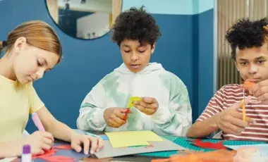 3 kids sitting at table and cutting paper