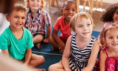 Group of young kids sit on floor rugs listening to a story