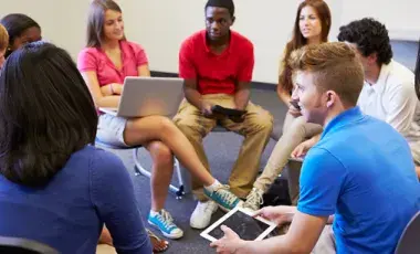 A group of teens sit in a circle for a Teen Council meeting.