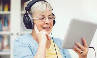 Adult woman with black headphones looking at a white tablet.