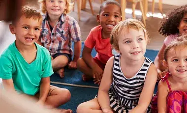 Children sitting down listening to someone off frame read them a story. 