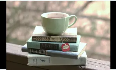Photo of a cup of tea on a pile of books outside. 