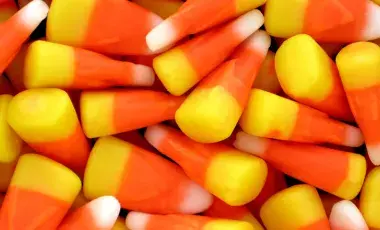 Bright, colorful candy corn pieces fill the image. Each piece has a yellow base, orange middle, and white tip, conveying a festive Halloween vibe.