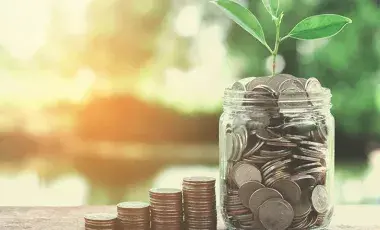 big jar of coins with four piles of growing coins 