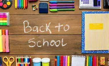 A variety of school supplies on top of a desk. "Back to School" is written in chalk