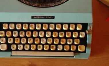 Typewriter and pen sit on a desk.