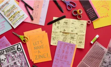 Paper, scissors, pens and paper booklets folded on a red background