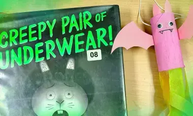 A pink bat craft with tissue paper is displayed beside spooky children's picture books.