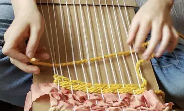 Cardboard lap loom on a child's lap. 