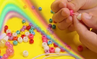 A hand stringing beads on a yellow background with a rainbow