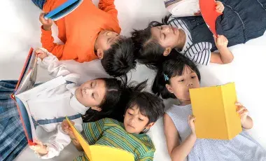Five children laying on their backs reading books in a circle.