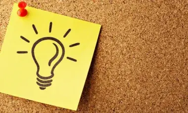 a post-it note with a lightbulb drawn on it is thumb tacked to a corkboard