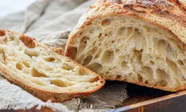 image of a loaf of sourdough bread with one slice cut off on a tan cloth on a cutting board. 