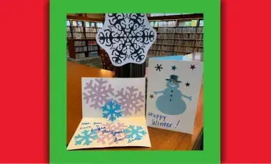 A paper snowflake and two paper greeting cards with images of snowflakes and a snowman.