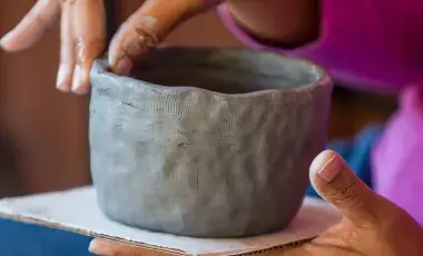 fingers shaping a small gray clay pot