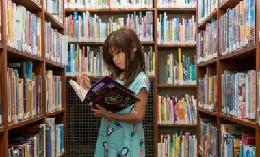 Standing girl, reading a book, surrounded by bookshelves