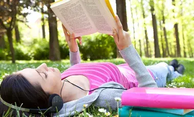 A girl lies on the grass, reading while wearing headphones
