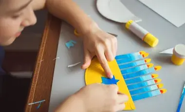A child decorating a Hanukkah menorah cut-out in shades of blue with nine candles lit.