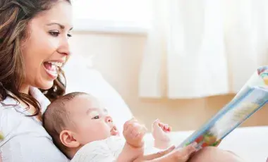 A woman holds a baby and a book