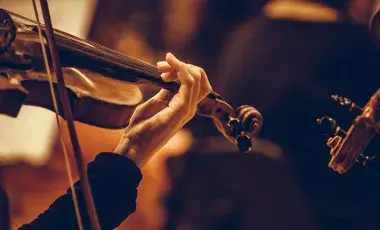 Hands of a musician holding onto a violin is shown performing. 