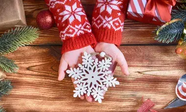 Child’s hands in a red and white sweater holding a wooden snowflake ornament.