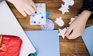 hands are making a snowflake card with cardmaking supplies around them