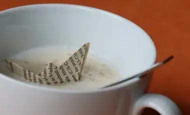 close up of an origami boat floating in a cup of coffee