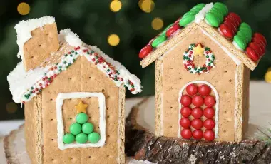 Two gingerbread houses made of graham crackers, white frosting, and various colorful candies are on display. 