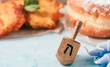 A dreidel beside blue candles, in front of fried snacks