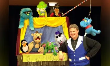 A puppet show performer poses with his puppets and puppet theater
