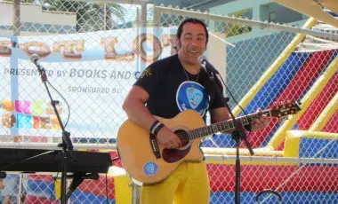 Image of artist, Teacher Davis, playing the guitar and singing on stage, at a festival.