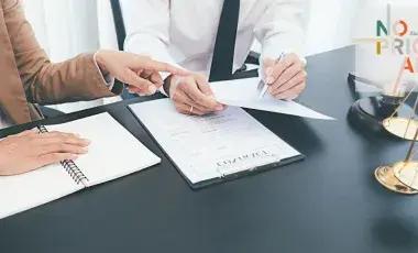 The hand of a person in a suit points to a document held by another person, next to a gavel and scales