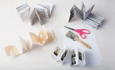 Several folded mini magazines (zines) are scattered throughout the table with a paintbrush and scissors shown. 