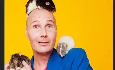 Christopher T. Magician in a blue coat against a yellow background holding guinea pigs.