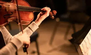 A person holding a violin while reading sheet music