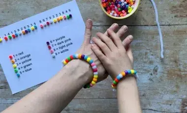 cup of beads, paper template describing which bead goes with which number, two hands wearing colorful beaded bracelets.