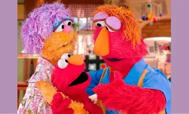 Sesame Street characters are in the photo with Elmo's parents giving him a hug and explaining something important to him. 
