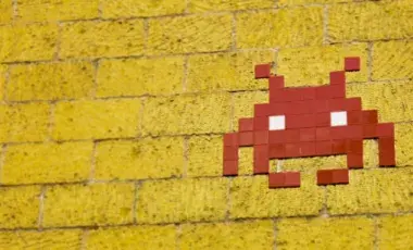 space invader made from red tiles on yellow brick wall