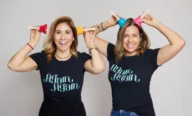 Two women smiling holding two instruments on eithe sides of their heads