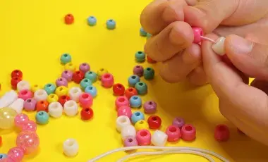 A child's hands putting beads through a piece of thread. 