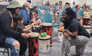 Music teacher working with child and mother playing drums in a group setting.