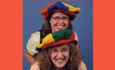 Two women standing together with colorful hats and stage costumes.